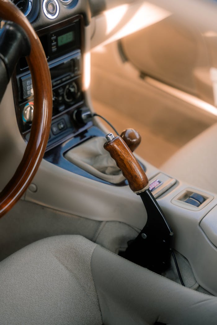 Close-up of a classic car interior featuring a sleek wooden gear lever and beige upholstery.