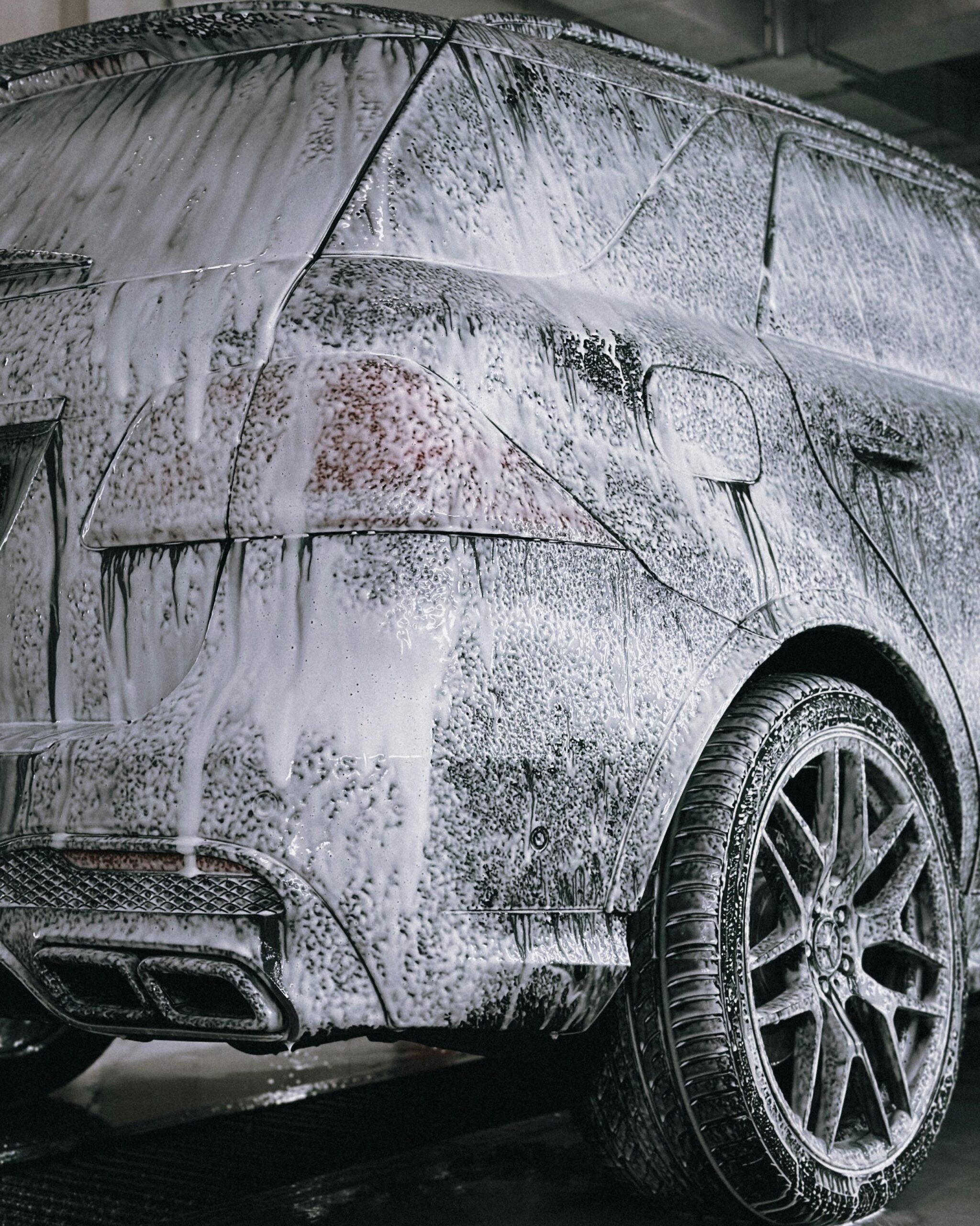 A premium SUV being cleaned with foamy soap in a detail car wash facility.